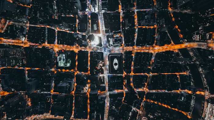 Vista aérea noturna de uma malha urbana densa, com as avenidas iluminadas em laranja